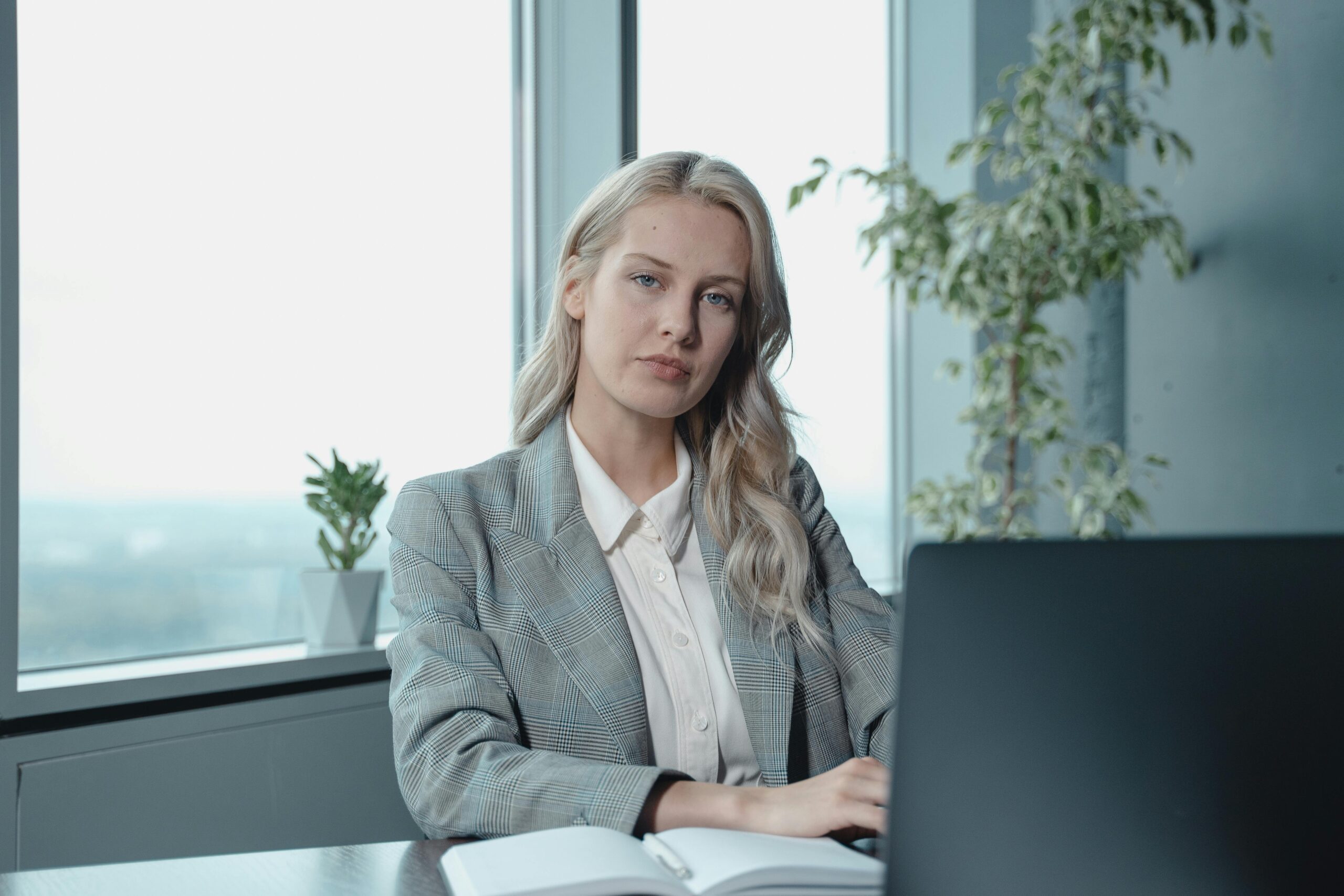 ABOUT Professional businesswoman at a desk in a bright office with a laptop and notebook.
